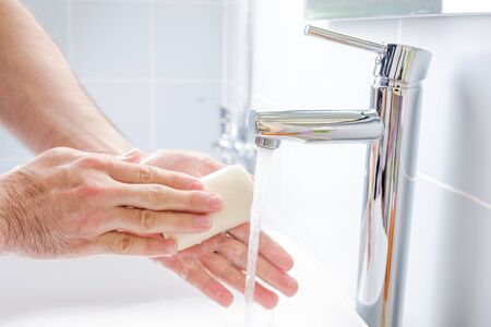 Washing hands with soap under running water in the bathroomの写真素材