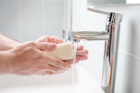 Washing hands with soap under running water in the bathroomの写真素材
