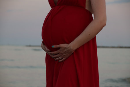 Pregnant woman in a red dress on the beach at sunsetの写真素材
