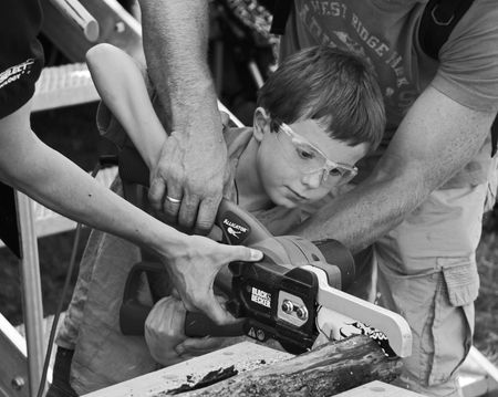 Bristol Balloon Fiesta, Bristol, UK 8th August 2009 a young boy is helped to use a wood cutting powertool by two menのeditorial素材