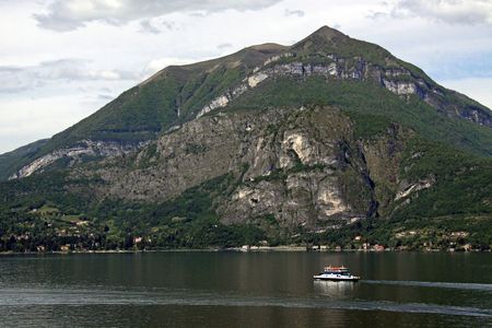 View of tree covered mountains and ferry boat and Lake Como in Italyの写真素材