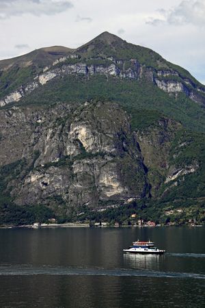 View of tree covered mountains and ferry boat and Lake Como in Italyの写真素材