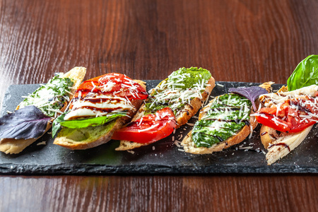 Italian bruschettes with mozzarella cheese, tomatoes, pesto sauce and parmesan cheese, on a black stone, on a wooden table. Copy space, selective focusの写真素材