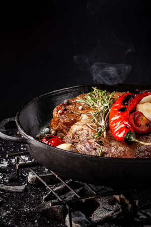 concept of the process of cooking meat. The steak is roasted on charcoal in a cast-iron frying pan, with spices, garlic, hot red pepper, squarish, thyme. image background. Copy space, selective focusの写真素材