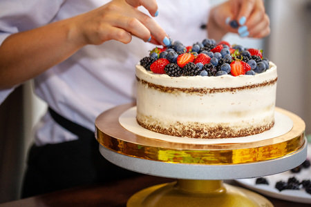 Girl chef cooks confectioner, decorates cake with forest berries. concept making without lactose cakes. Copy space, selective focusの写真素材