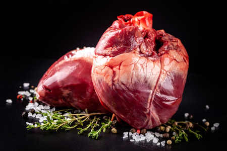 Beef raw heart on a black background with rosemary and spices.の写真素材