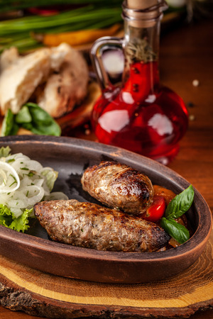 Uzbek traditional oriental cuisine. Lulya kebab from ground beef with pickled onion, salad, cherry tomatoes in a dish of red clay. Background image. Copy space, selective focusの写真素材
