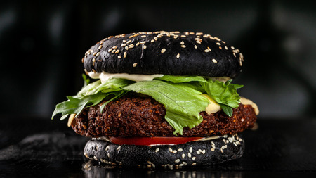 Vegetarian black burger with cutlet peas falafel, tomato, cucumber, rucola salad and French fries. on a black background. Copy space, selective focusの写真素材