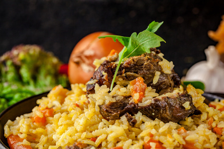 Uzbek Oriental cuisine. Pilaf in a cast-iron frying pan made of lamb. next to the vegetables on a black table. selective focusの写真素材