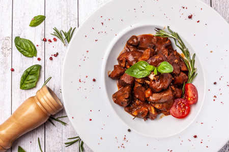 The liver of foie gras and juicy beef meat in a spicy tomato sauce with basil and cherry tamata in a chalk plate on a white, angled table. concept of a beautiful serving of food in a restaurantの写真素材