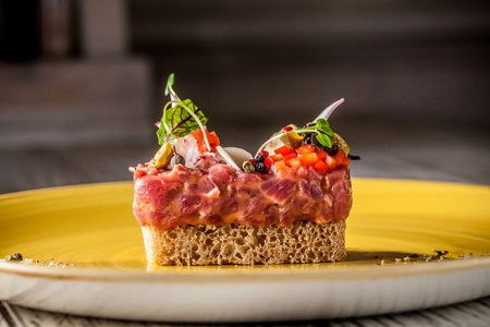 The concept of haute cuisine. Tartar from raw veal with marinade, sauce, with vegetables, with bread, with micro green, on a yellow ceramic plate. Beautiful serve in the restaurant.の写真素材