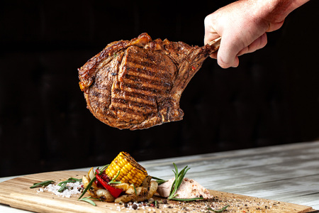 A large roasted piece of mutton steak, pork, veal or beef on bones cooked on an air fryer, in the hands of the chef's chief, a background image on a black background.の写真素材