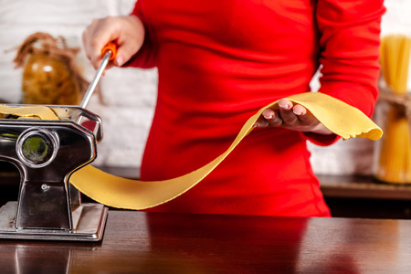 Step by step. Manual process of making Italian pasta Fettuccine. Home pasta with Pasta Maker. Flour, semola di grano duro, eggs, tomatoes, basil lie on a wooden table. For the recipe.の写真素材