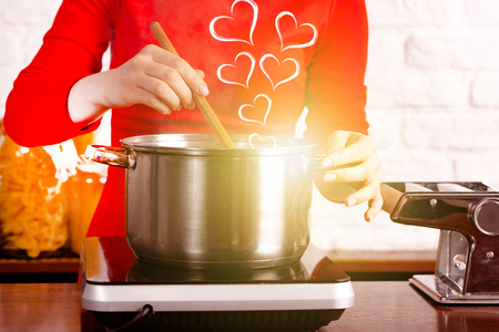 A beautiful young girl, woman or housewife in her home kitchen, cooks breakfast, lunch or dinner for her beloved husband, stirring soup. Concept is cooking with love. Background image. Copy spaceの写真素材