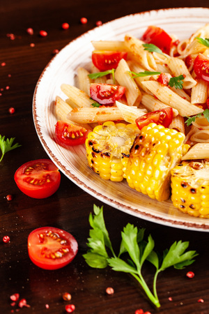 Italian traditional cuisine. Penne pasta with tomato sauce and tomatoes, with parsley and grilled corn. Background image on a wooden table. copy space, top viewの写真素材