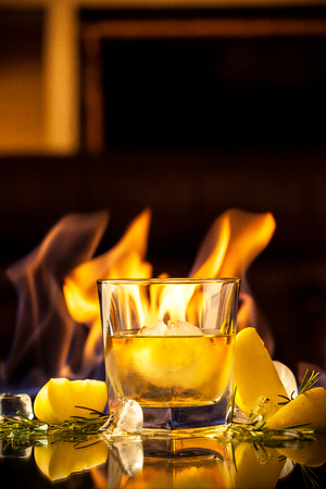 Expensive whiskey in a glass with a ball of ice, against the background of fire, on a reflective black surface. concept background image for a bar, restaurant, cafe. Copy spaceの写真素材
