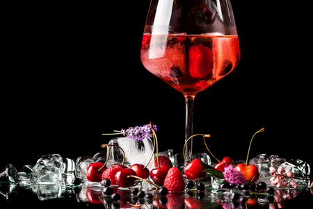 berry cold cocktail with alcohol in a glass crystal glass on a black background with berries, raspberries, strawberries, cherries, with ice. background image. Copy space, selective focus