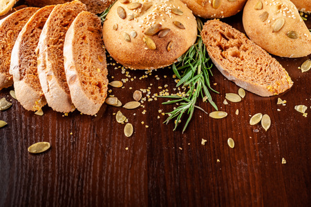 Homemade wholemeal tomato bread with basil and pumpkin seeds, baguette, buns, lie on a wooden table....