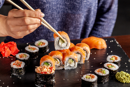 The concept of Japanese and Chinese cuisine. The girl in the restaurant has wooden chopsticks sushi and rolls.の写真素材