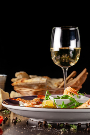The concept of Italian cuisine. Tiger prawns on rice chips in a creamy sauce. Arugula salad and lemon. On the table is a glass of red wine. beautiful serving in the restaurantの写真素材