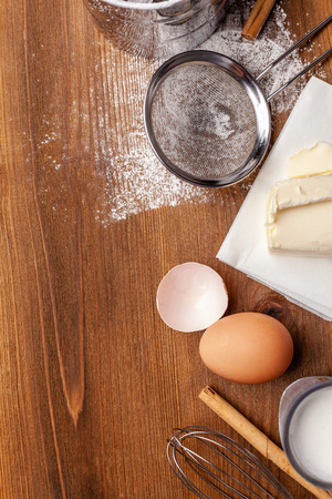 Kitchen, pastry inventory lies on the wooden table. Butter, eggs, wooden spoons, whisk, flour, milk. Top view with copy space, mockup for menu, recipe for culinary classes. Baking background Imageの写真素材
