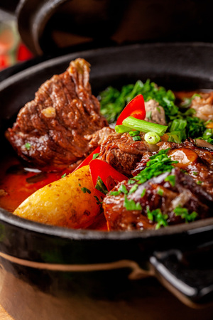 The concept of Serbian cuisine. Juicy baked beef in its own juice with potatoes, vegetables and greens. Serve in an iron fire on a wooden board.の写真素材
