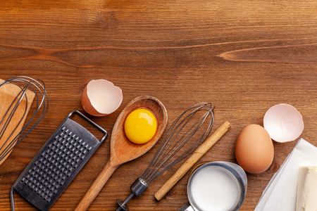 Kitchen, pastry inventory lies on the wooden table. Butter, eggs, wooden spoons, whisk, flour, milk. Top view with copy space, mockup for menu, recipe for culinary classes. Baking background Imageの写真素材