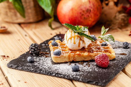 Belgian waffles with a scoop of ice cream, fresh berries raspberries, blackberries, blueberries and mint. Dusted with icing sugar and poured over caramel sauce. selective focusの写真素材