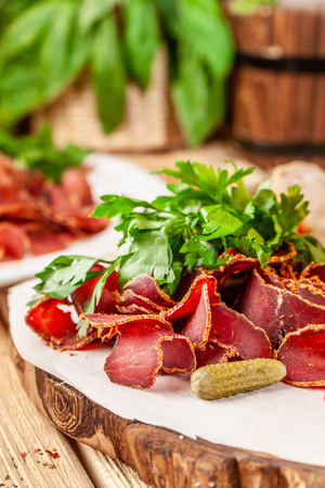 Concept of Georgian restaurant. A glass of black beer with foam stands on a wooden table, next to it is a beer snack, dried sausage, basturma, smoked meat and parsley with dill.の写真素材