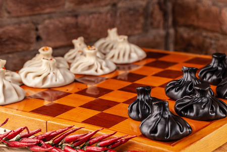 concept of Georgian cuisine. black and white khinkali stand on a chessboard. female hand takes khinkali. khinkali with barinas, veal and cheese.の写真素材