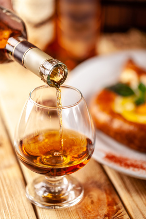 Concept of Georgian restaurant. A girl pours Georgian brandy from a bottle into a glass. On a wooden table is hachipuriの写真素材