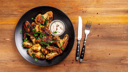 Baked chicken wings in Mexican with curry seasoning and parsley on a black plate, on a wooden background. side view, copy space, top viewの写真素材