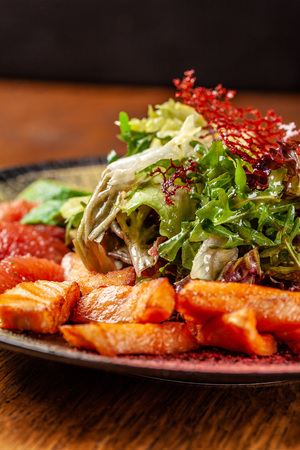 Modern Arabic cuisine in 2019. Asian salad of fried salmon, avacado, grapefruit and salad mix, with honey sauce. Serving dishes in a restaurant in a black plate with oriental spices.の写真素材