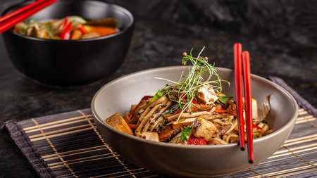 The concept of Japanese cuisine. Chinese noodles with chicken, grilled vegetables, and tofu in unagi sauce. Serving Asian dishes in the restaurant in a plate on a bamboo mat. Top view, copy spaceの写真素材