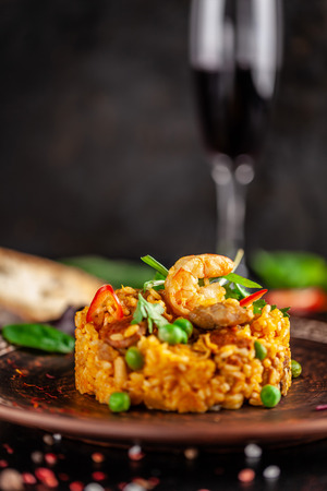 Concept of Spanish cuisine. Paella with seafood and shrimps, with green peas in a clay plate. A glass of cool wine is on the table. background image, copy spaceの写真素材