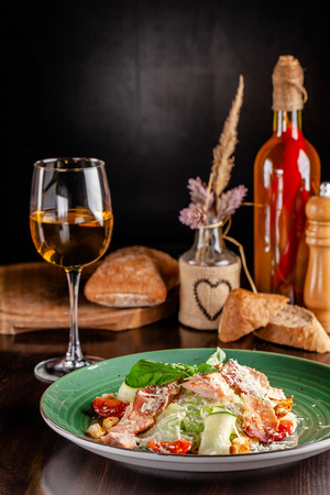 The concept of Italian cuisine. Caesar salad with salmon, lettuce mix, cherry tomatoes and parmesan cheese. A glass of white wine on the table. Serving dishes in the restaurantの写真素材