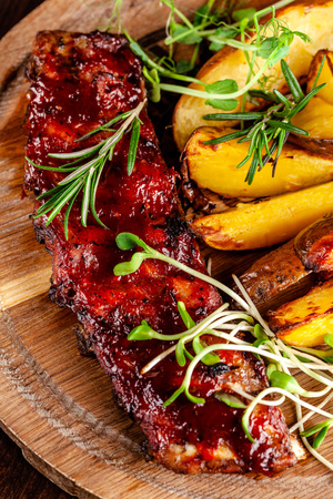 Grilled ribs with potatoes in a rustic style with barbecue sauce. Serving dishes in the restaurant on a wooden board. A glass of cool wine. Background image close up. copy spaceの写真素材
