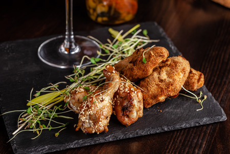 The concept of Italian cuisine. Snack to beer. Glazed chicken legs and chicken wings, breaded. Serving dishes in the restaurant on a black stone slate. Copy spaceの写真素材