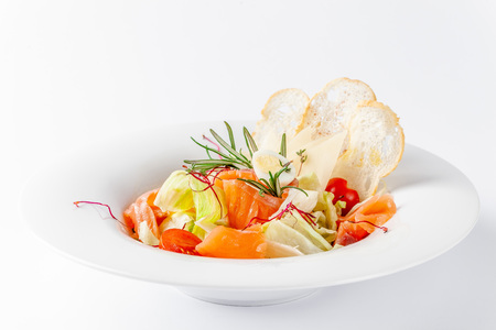 American cuisine concept. Caesar salad with salmon. White plate on a white background. Image for a menu of restaurants or cafes.の写真素材