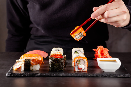 The concept of Japanese cuisine. A girl holds a red Chinese chopsticks and eat sushi in a restaurant. background image. Popular Japanese food. copy spaceの写真素材