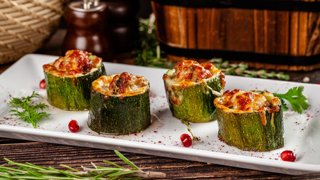 Concept of Georgian cuisine. Stuffed zucchini with minced lamb meat, Suluguni cheese. Serving dishes in a restaurant on a white plate with pomegranate. copy space, background imageの写真素材