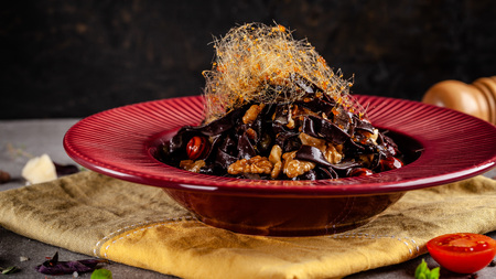 The concept of Italian cuisine. Sweet Pasta papardelle with walnuts nuts and candied fruit. Cocoa black paste. Serving dishes in a restaurant in a red plate. copy spaceの写真素材