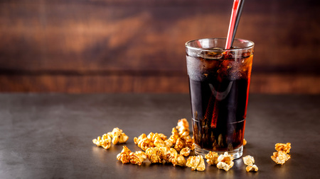 The concept of food for the cinema, for watching a movie. Cold cola drink with ice in a glass filled with popcorn. Closeup, background image. copy the text.の写真素材