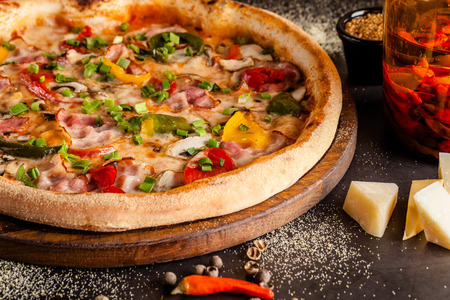 Concept Italian cuisine. A real pizza with vegetables and ham, bacon and parmesan cheese. The ingredients on the table. Red wine in a glass on the table. Closeup, background imageの写真素材