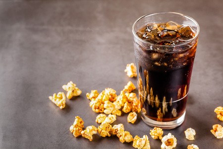 The concept of food for the cinema, for watching a movie. Cold cola drink with ice in a glass filled...