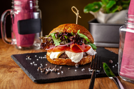 Concept of Italian home cooking. Burger with beef and pork meat cutlet, mozzarella cheese, salami sausage, parma, arugula and lettuce mix. Beautiful serving in restaurant. の写真素材