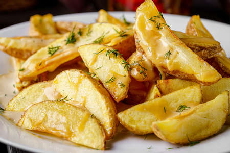 Country style potatoes with melted cheese. Serving food in a restaurant on a white plate. Background...