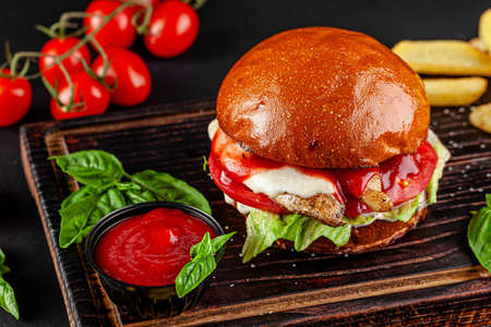 American cuisine. Burger with chicken, cheese, tomatoes, lettuce and tomato sauce. Serving the dish on a wooden board.の写真素材