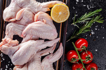 Raw meat. Chicken wings lie on a wooden board with vegetables and spices on a black background. background image, copy space textの写真素材