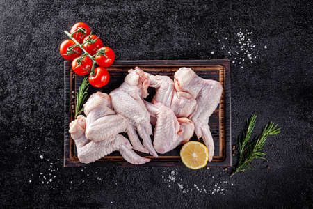 Raw meat. Chicken wings lie on a wooden board with vegetables and spices on a black background. background image, copy space textの写真素材